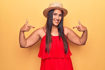 Young beautiful brunette woman wearing summer hat and dress looking confident with smile on face, pointing oneself with fingers proud and happy.