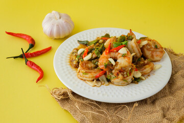 Stir-fried shrimp with chilli with garlic and chilli and spoon and fork with yellow background.