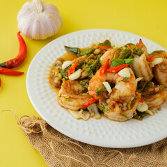 Stir-fried shrimp with chilli with garlic and chilli and spoon and fork with yellow background.