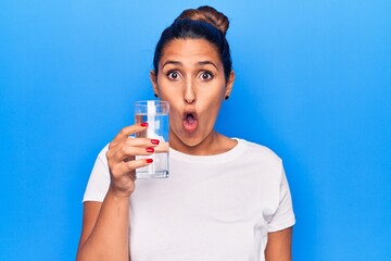 Young beautiful brunette woman drinking glass of water scared and amazed with open mouth for surprise, disbelief face