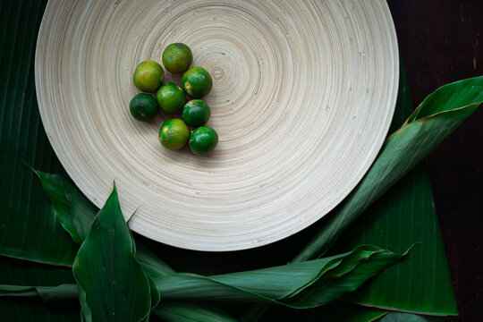 Fresh local calamansi or limau kasturi (citrus microcarpa) on a wooden plate.