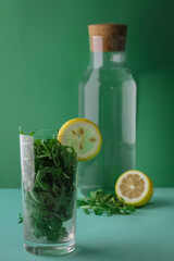 Green vegetable smoothie, cocktail of greens and lemon slice in front of trendy deep green background