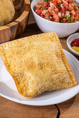 .Typical Brazilian snack called Pastel. Accompanied by vinaigrette and pepper on a wooden background