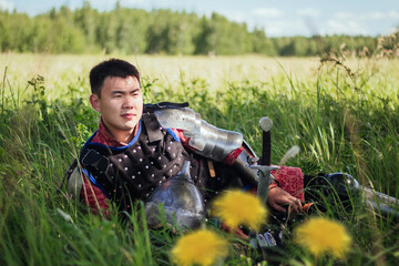 A medieval Asian warrior in armor is resting while sitting in tall grass.