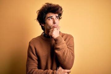 Young handsome man wearing casual shirt and sweater over isolated yellow background Thinking worried about a question, concerned and nervous with hand on chin