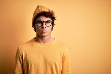 Young handsome man wearing casual t-shirt and glasses over isolated yellow background skeptic and...
