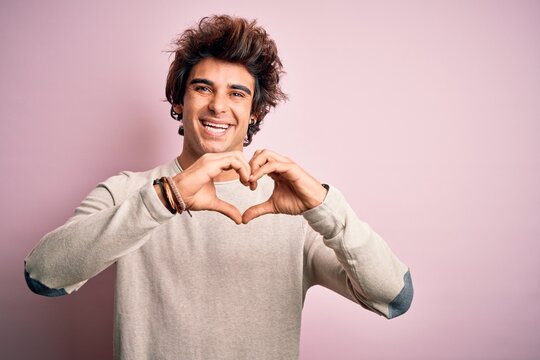 Young handsome man wearing casual t-shirt standing over isolated pink background smiling in love doing heart symbol shape with hands. Romantic concept.