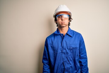 Young constructor man wearing uniform and security helmet over isolated white background puffing cheeks with funny face. Mouth inflated with air, crazy expression.