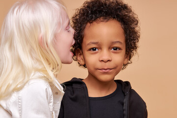 friendly diverse children play, tell stories and secrets to each other isolated in studio. girl with albinism syndrome share secret with african boy