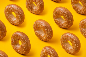 Colorful pattern with round bread bagels with sesame seeds on yellow background