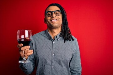 Young african american afro sommelier man with dreadlocks drinking glass of wine with a happy face standing and smiling with a confident smile showing teeth