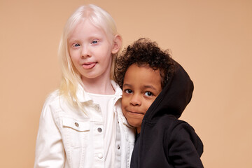 beautiful albino girl with little afro multiracial boy isolated, girl hug her black friend. girl show tongue at camera. unusual natural beauty, albinism and people diversity concept