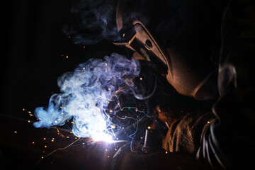 Welder at work. Man in a protective mask. The welder makes seams on the metal. Sparks and smoke when welding.