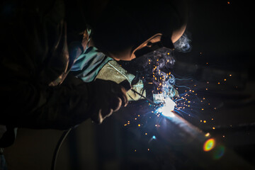 Welder at work. Man in a protective mask. The welder makes seams on the metal. Sparks and smoke...