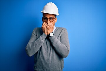 Young handsome african american engineer man with dreadlocks wearing safety helmet looking stressed and nervous with hands on mouth biting nails. Anxiety problem.