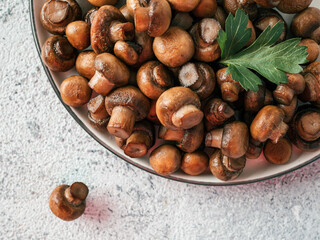 Ready-to-eat fried mini champignons on plate with copy space. Perfect mini mushrooms heap on plate over gray cement background. Natural day light. Top view or flat lay.