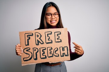 Asian girl asking for rights holding banner with free speech message over white background very happy pointing with hand and finger