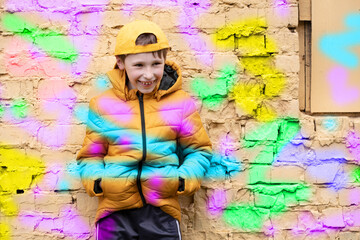 Child in graffiti. The boy is standing against a brick wall in fashionable clothes and a baseball cap, outlined with bright colors.