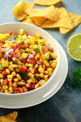 Mexican Corn Salsa in white bowl with lime and tortilla chips. Healthy food