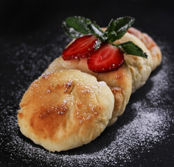 Russian and ukrainian cuisine. Cheesecakes on a black background with berries and mint. Cottage cheese pancakes. Background image, copy space