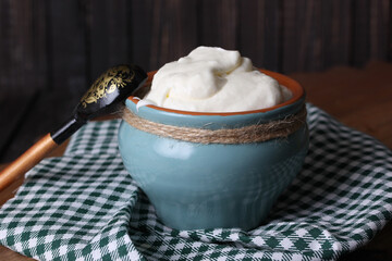 Homemade sour cream in a pot with a spoon on an old wooden background. Rustic. Milk products. Background image, copy space