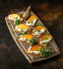 Fototapeta na wymiar Cottage cheese and nectarine wedges on melba toast appetizers drizzled with runny honey and served with cress salad microgreen. Healthy party finger food