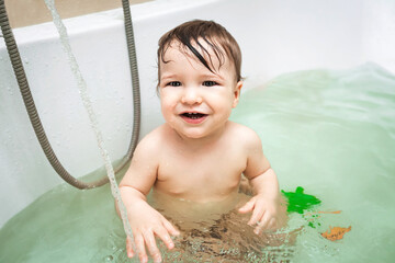 Cute happy little baby boy taking bath with toys, child's hygiene, healthy lifestyle, carefree childhood concept