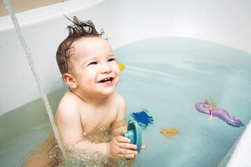 Cute happy little baby washing and playing in bathroom with colorful plastic toys. child's hygiene, healthy skin and body, happy lifestyle, carefree childhood concept