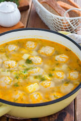 Potato soup with meatballs in an enameled pan on a wooden table, selective focus