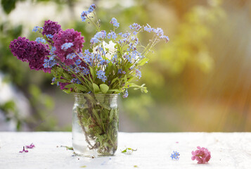 Spring or summer background. A bunch of bright flowers in a glass jar lit by sunlight. Beautiful flowers on a green background.