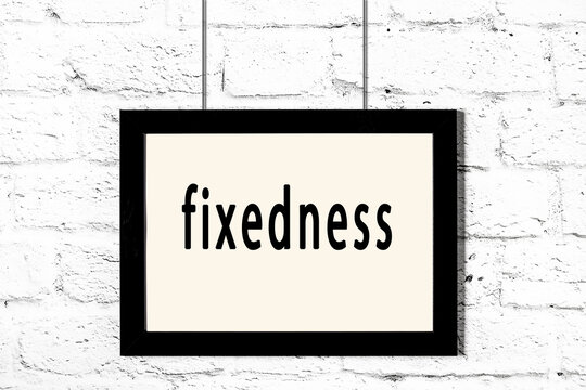Black frame hanging on white brick wall with inscription fixedness