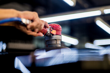 The worker polishes a car with the electric tool.
