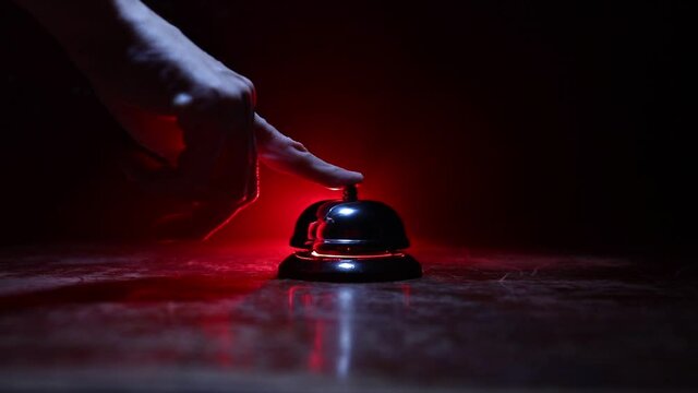 Calling service bell on wooden table with toned lights on dark background. Hotel reception bell, Hand ringing in service bell , selective focus