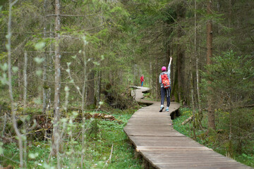Travel. Young girl traveler with orange backpack and children walking on a wooden bridge in nature...