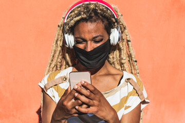 Yound african girl with blond dreadlocks using mobile phone while listening playlist music - Trendy...