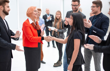 Two business people shaking hands in front of their colleagues