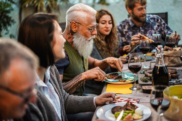 Family eating at barbecue home party dinner - Different age of people having fun at bbq meal in villa backyard - Summer lifestyle and food concept - Main focus on hipster man's face