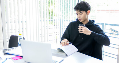 Fototapeta premium Asian man students read books and use computer notebook to find information for work and online studies.