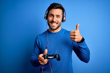 Young handsome gamer man with beard playing video game using joystick and headphones happy with big...