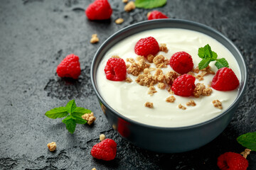 Greek yogurt with granola and raspberry in black bowl. Healthy breakfast food or snack