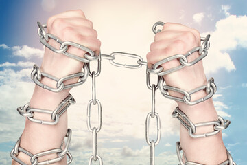 Two hands shackled a metal chain on blue sky background. Freedom concept