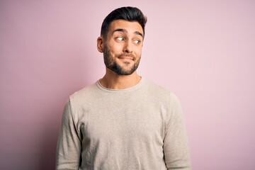 Young handsome man wearing casual sweater standing over isolated pink background smiling looking to the side and staring away thinking.