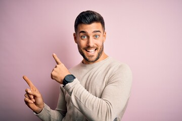 Young handsome man wearing casual sweater standing over isolated pink background smiling and looking at the camera pointing with two hands and fingers to the side.
