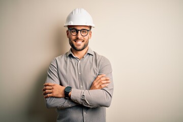 Young architect man wearing builder safety helmet over isolated background happy face smiling with crossed arms looking at the camera. Positive person.