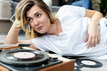 young blonde girl listens to vinyl records on an old record player lying on the floor