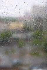 window glass in drops from spring rain on a blurred background of houses and trees