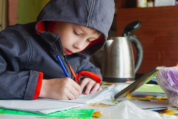 A European teen boy in a jacket sits at a table and does homework.