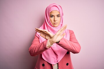 Young beautiful girl wearing muslim hijab standing over isolated pink background Rejection expression crossing arms and palms doing negative sign, angry face