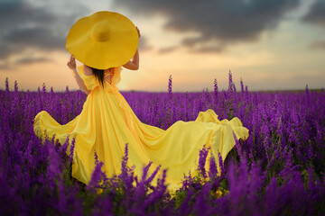 Summer mood. A woman in a luxurious yellow dress is standing in a purple flowering field with her...