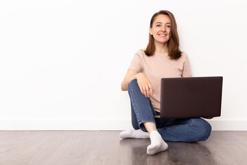 Smiling young woman sitting on the floor with laptop computer over white background, work from home, online education concept.